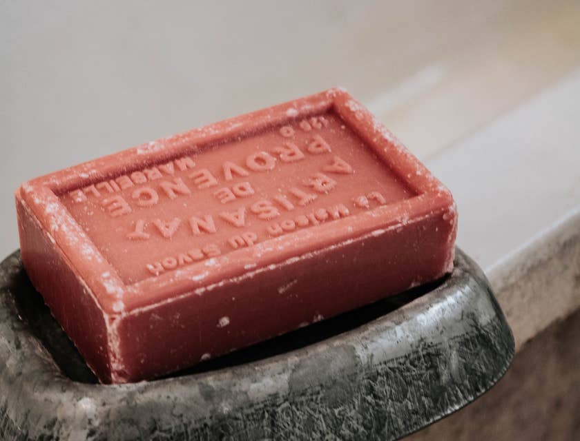 Artisan soap bar in a soap holder on the edge of a bathtub.