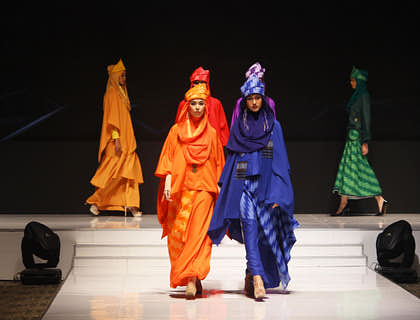 Models show off designer modest clothing on a runway.