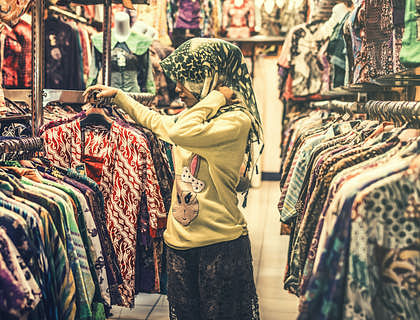 Mujer con mascada en la cabeza entre colgadores de ropa en un bazar de ropa usada.