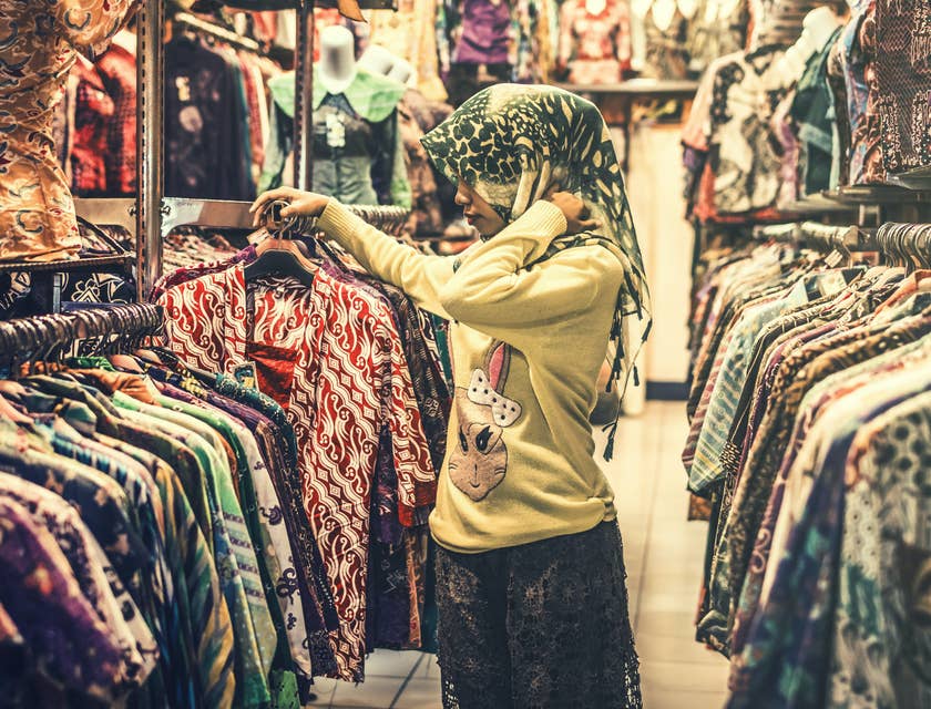 Mujer con mascada en la cabeza entre colgadores de ropa en un bazar de ropa usada.