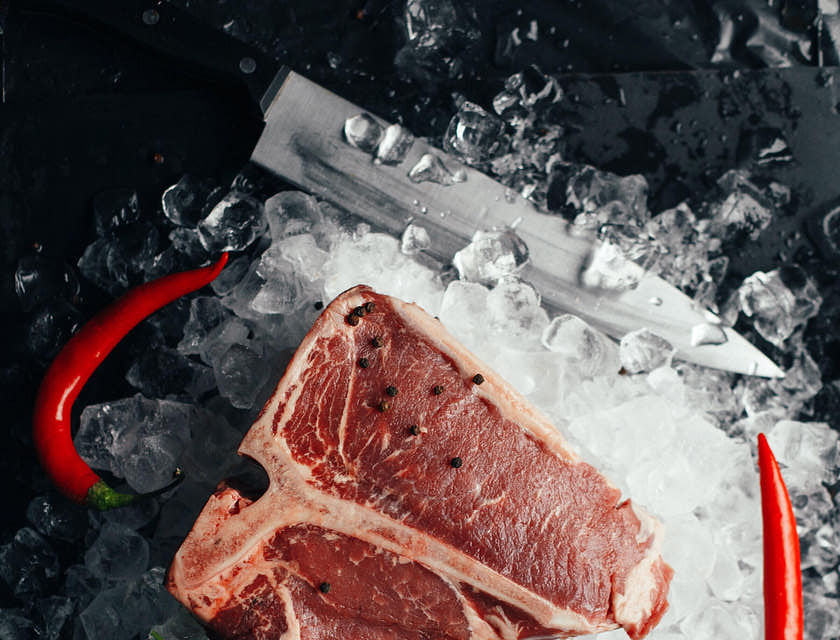 Un T-bone steak sobre una cama de hielo con dos chiles rojos, un manojo de cilantro y un cuchillo a su alrededor, en una boutique de carnes.