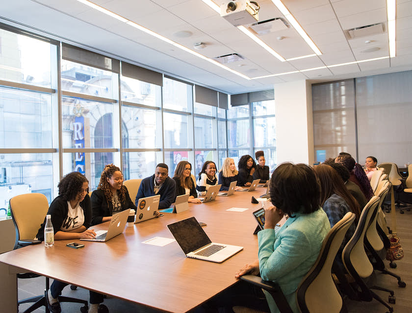 Sala de juntas de una consultora con personas reunidas y laptops sobre la mesa.