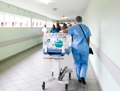 Una enfermera transportando a un bebé en una incubadora en un grupo de enfermería.