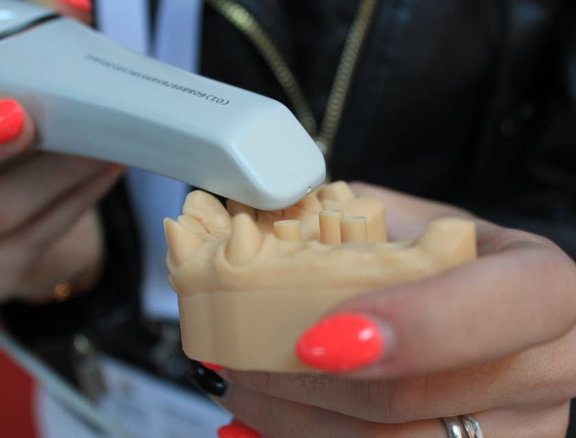 Empleada con las uñas pintadas de naranja sosteniendo una prótesis dental y un instrumento de laboratorio dental.