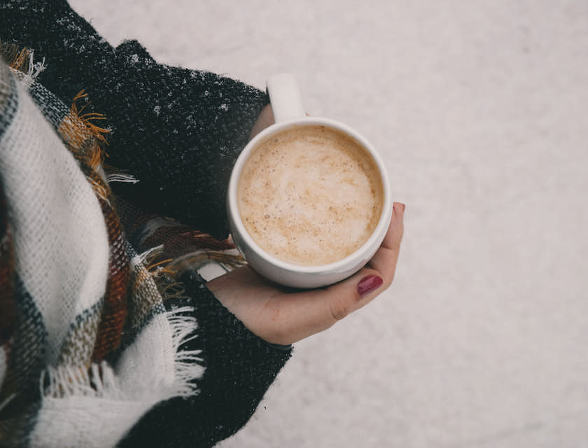 Una mujer sosteniendo una taza con atole con nieve de fondo en un negocio de atole.