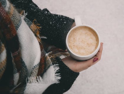 Una mujer sosteniendo una taza con atole con nieve de fondo en un negocio de atole.