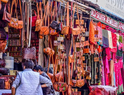 Negocio de carriel con carrieles exhibidos colgando del techo en un mercado turístico y dos personas viendo los productos