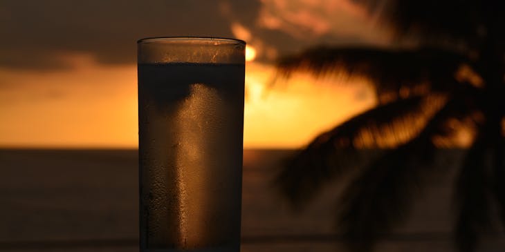 Una chicha fría servida en un vaso de un negocio de chicha con una palmera y la puesta de sol de fondo.