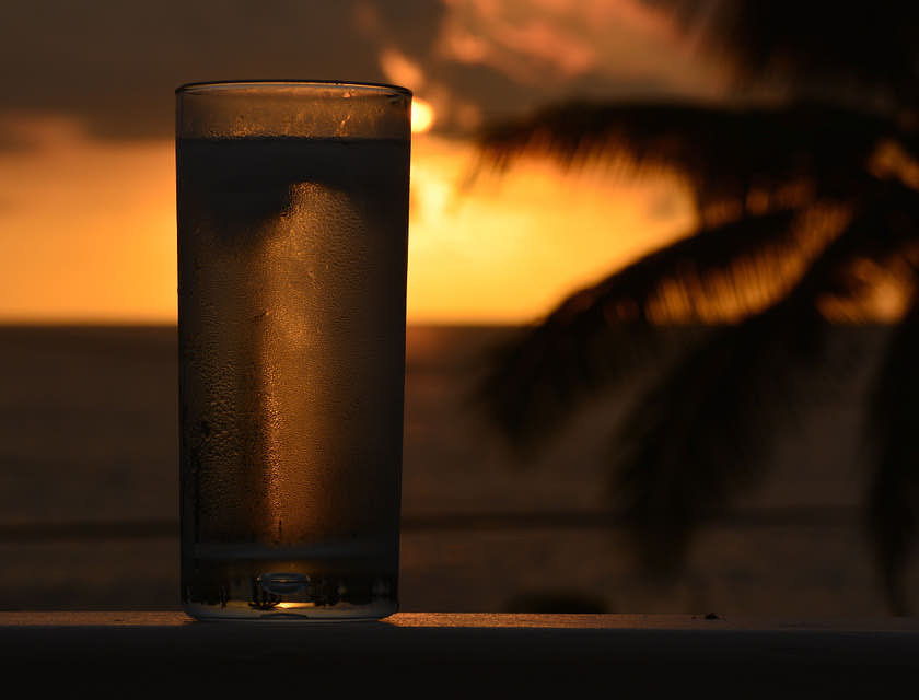 Una chicha fría servida en un vaso de un negocio de chicha con una palmera y la puesta de sol de fondo.