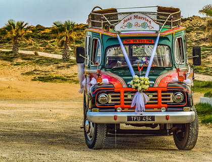 Una chiva pintada y adornada con arte colombiano en una calle frente a un negocio de chivas