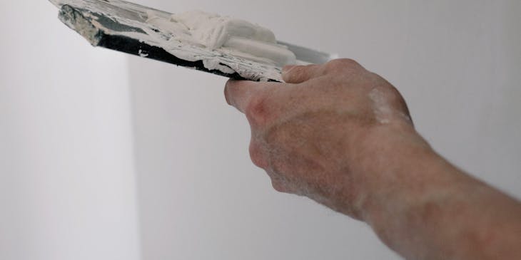Manos de un yesero con una espátula flexible y una espátula tapizadora aplicando yeso en un muro en un negocio de yesero.
