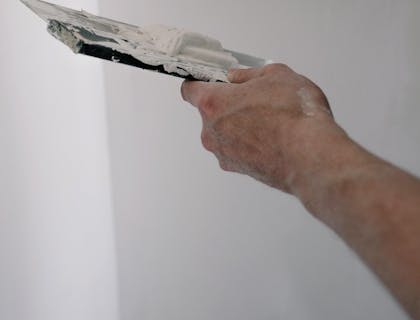 Manos de un yesero con una espátula flexible y una espátula tapizadora aplicando yeso en un muro en un negocio de yesero.