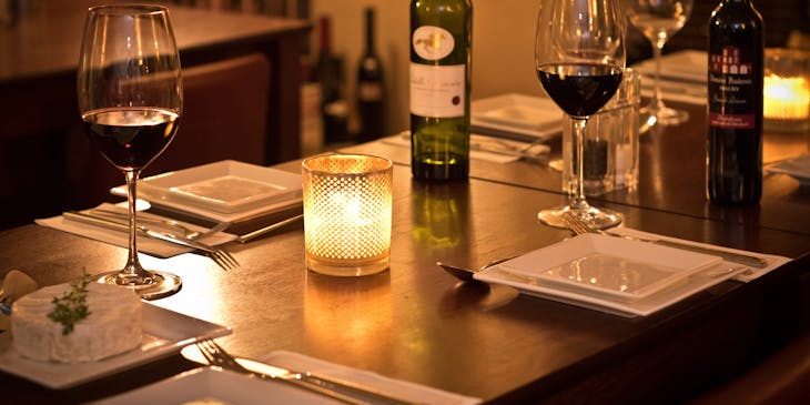 Table mise avec assiettes blanches carrées, verres de vin et camembert