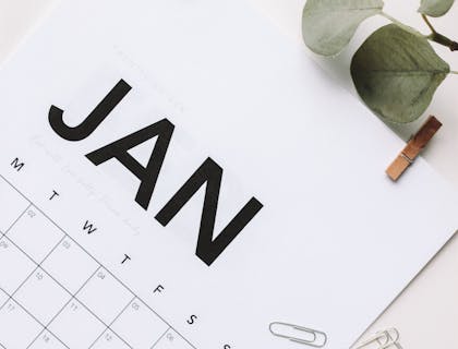 Una página de calendario con hojas verdes secas, clips y envoltorios de papel marrón esparcidos por la superficie en un negocio de trabajos ocasionales.