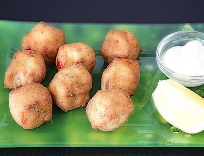 Accras de morrue sur un plat rectangulaire accompagnés d'un sauce blanche et un morceau de citron