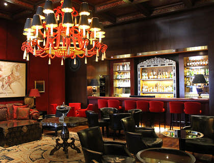 Eine Lounge mit roten Stühlen, Ledersesseln, einem Kronenleuchter und einer Bar.