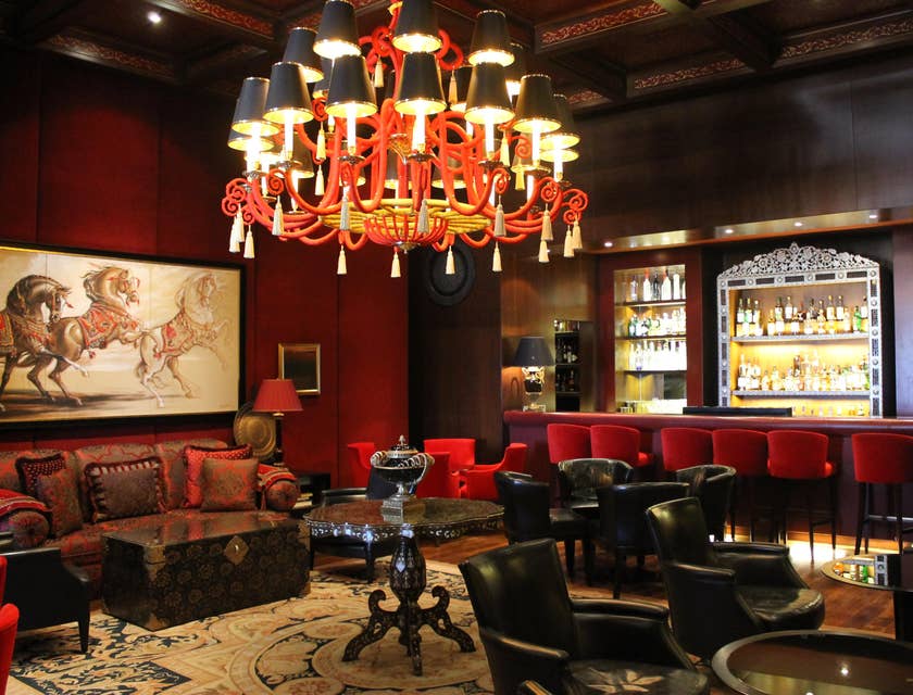 Eine Lounge mit roten Stühlen, Ledersesseln, einem Kronenleuchter und einer Bar.