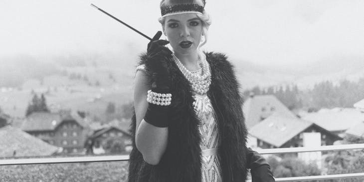 A black and white image of a woman in flapper dress holding a cigarette.