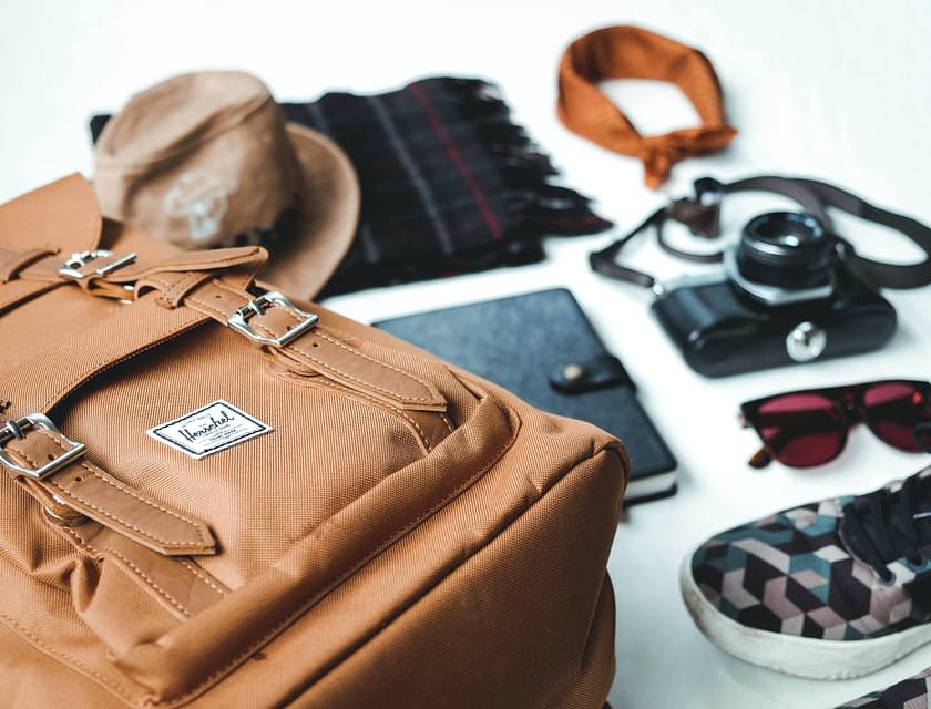 Eine schicke Ledertasche, ein Hut, ein Schal und andere Accessoires liegen auf einer weißen Oberfläche.