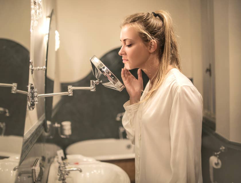 Una mujer examinando su rostro en un espejo de un negocio de tratamiento para el acné.