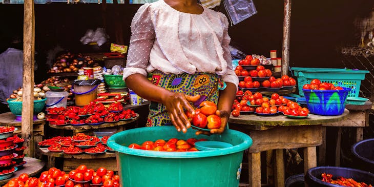 African woman holding tomatoes in front of her stall