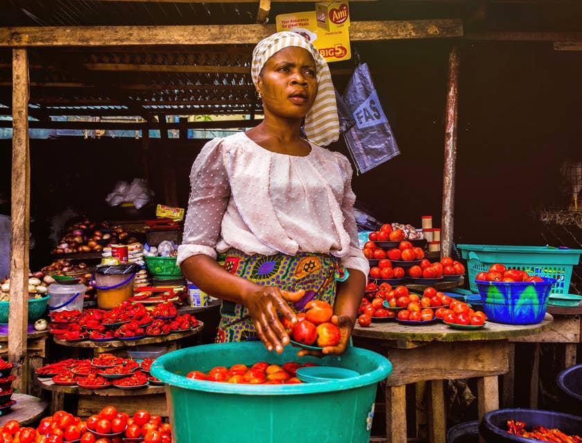 Femme africaine tenant des tomates devant son étalage.