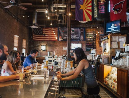 Una mujer tomando la orden de sus clientes detrás de la barra de un bar americano.