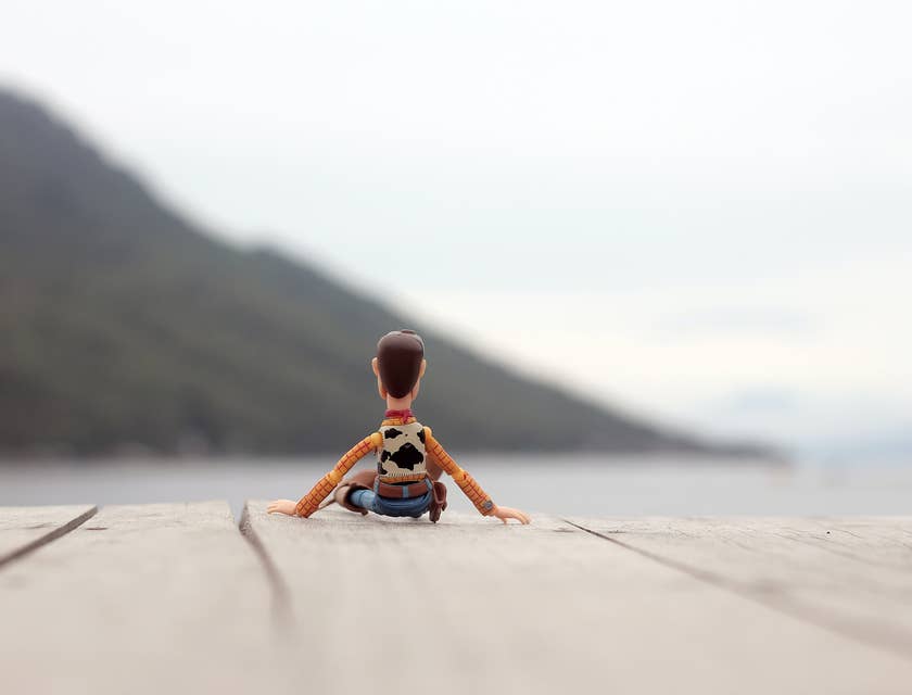 Un pupazzetto di Woody di Toys Story seduto su un pavimento di legno con vista sul mare.