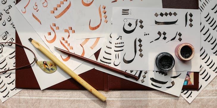 Arabic calligraphy art with calligraphy instruments displayed on top of papers.