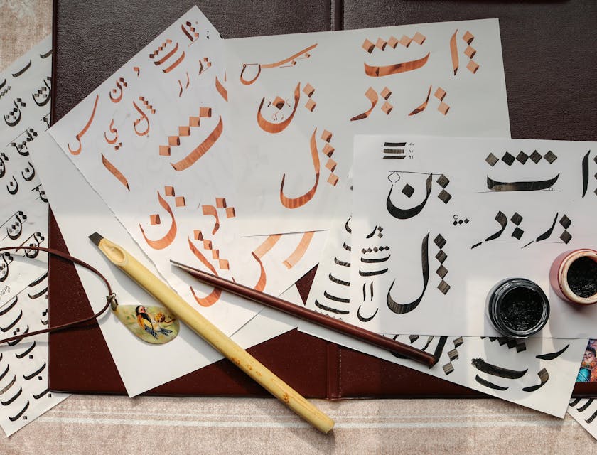 Arabic calligraphy art with calligraphy instruments displayed on top of papers.