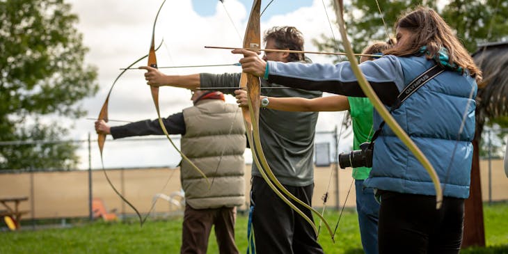 A group of people aiming their bows and arrows during an archery class.