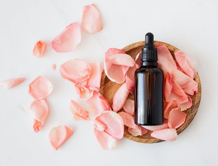 Difusor de aromaterapia sobre pétalos rosas en una superficie blanca.
