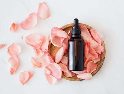 Un flacon d'aromathérapie sur des pétales de rose dans une coupelle.
