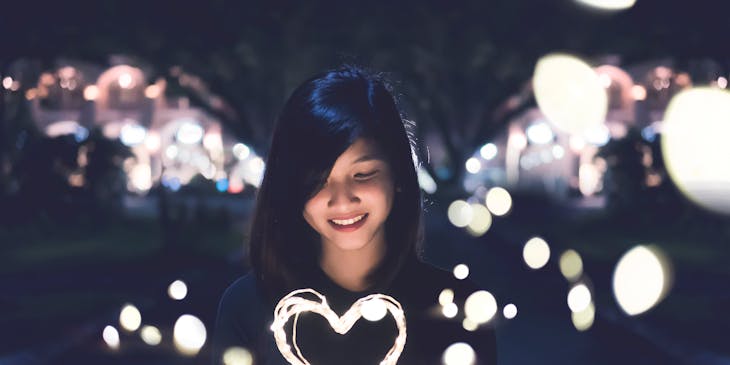 Asian woman holding a heart made from fairy lights.