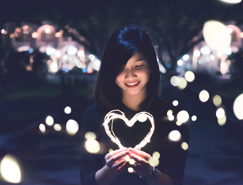 Una donna asiatica che regge in mano un cuore fatto con delle luci.