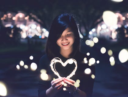 Una mujer asiática sosteniendo un corazón hecho de luces en la noche en una feria.
