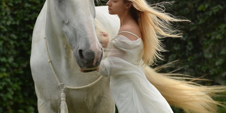 A woman in a white dress standing next to a white horse.
