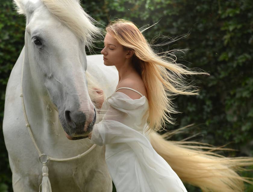 Femme en robe blanche se tenant à côté d'un cheval blanc.