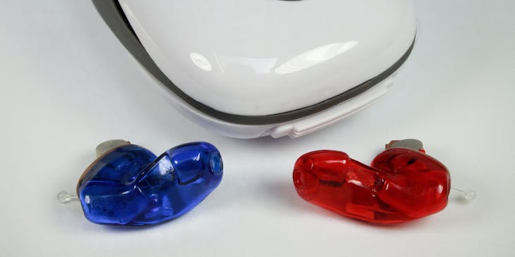 Blue and red hearing aids set in front of a white hearing aid case.