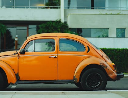 Volkswagen Beetle de color naranja en una calle afuera de una empresa de seguros de auto.
