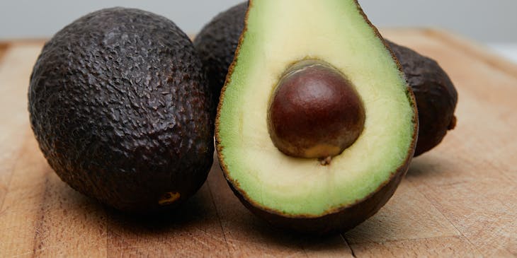 Three avocados on a wooden table.