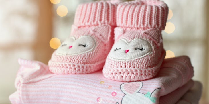 Pink baby booties ontop of folded baby clothes.