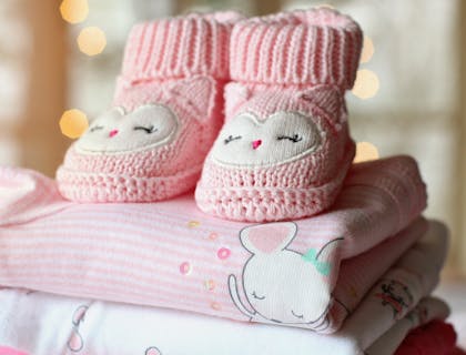 Botinhas de bebê em cima de roupas de bebê dobradas.
