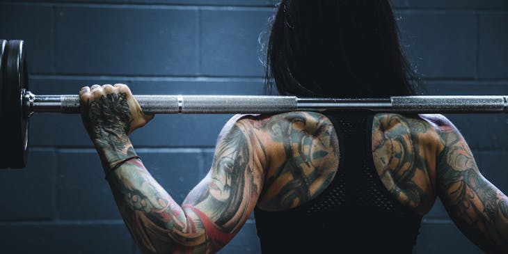 A badass woman with tattoos holding a barbell.