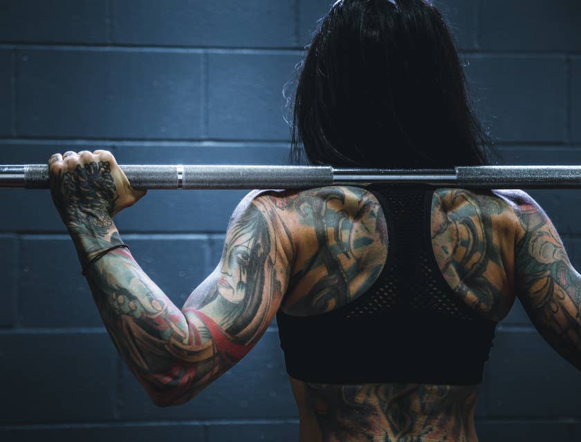 Femme badass avec des tatouages tenant une barre d'haltère.