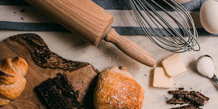 Baking tools, ingredients, and products on a wooden chopping board and blue and white dish towel.