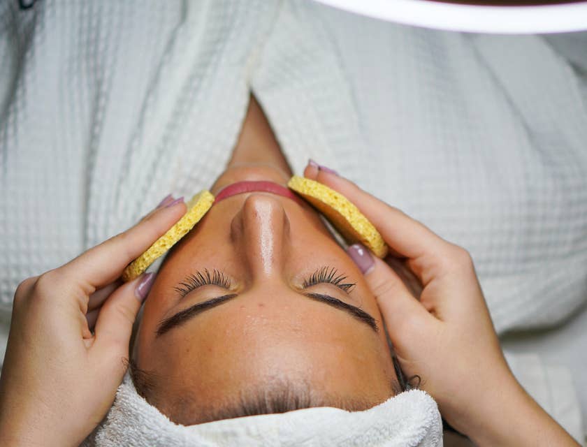 A woman with a white towel on her head having a facial at a beauty bar.
