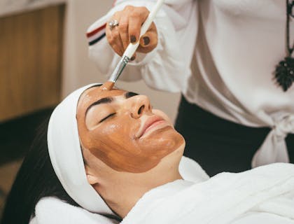 Una mujer recibiendo un facial de lodo en un centro de belleza.