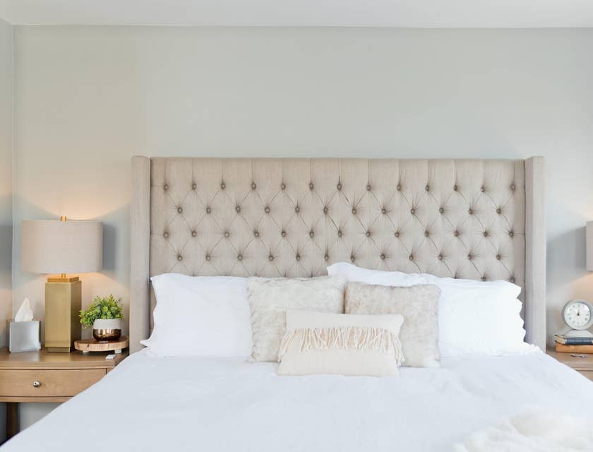 A bed with a beige headboard and white linen purchased from a bedding business.