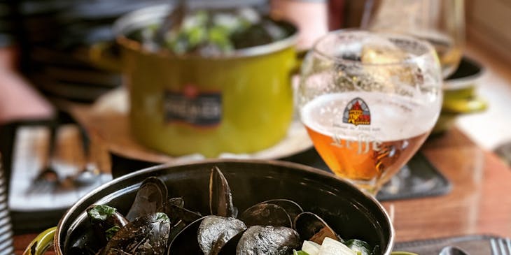 Belgian mussel dish in a pot beside glass of wine.